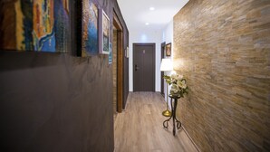 A hallway with wooden flooring, a door labeled '5', and a wall-mounted lamp with a flower arrangement. - Hotel Tergeste (Trieste)