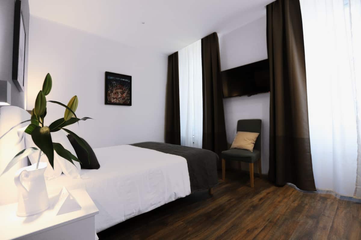 A hotel room with a bed, a chair, a plant, and a painting on the wall.
