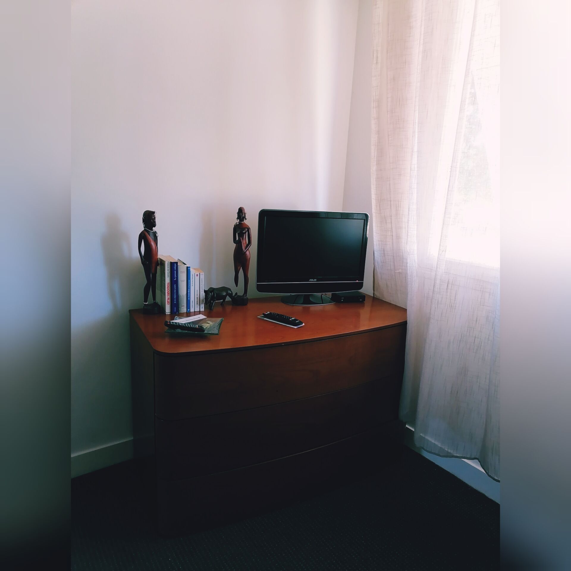 Une pièce comprenant un bureau en bois, un téléviseur et deux statuettes.