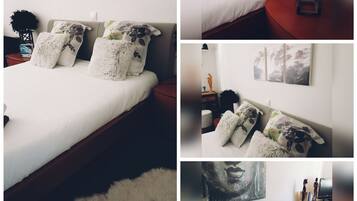A bedroom with a bed, fluffy pillows, a nightstand, a lamp, a wall-mounted painting, and a statue.
