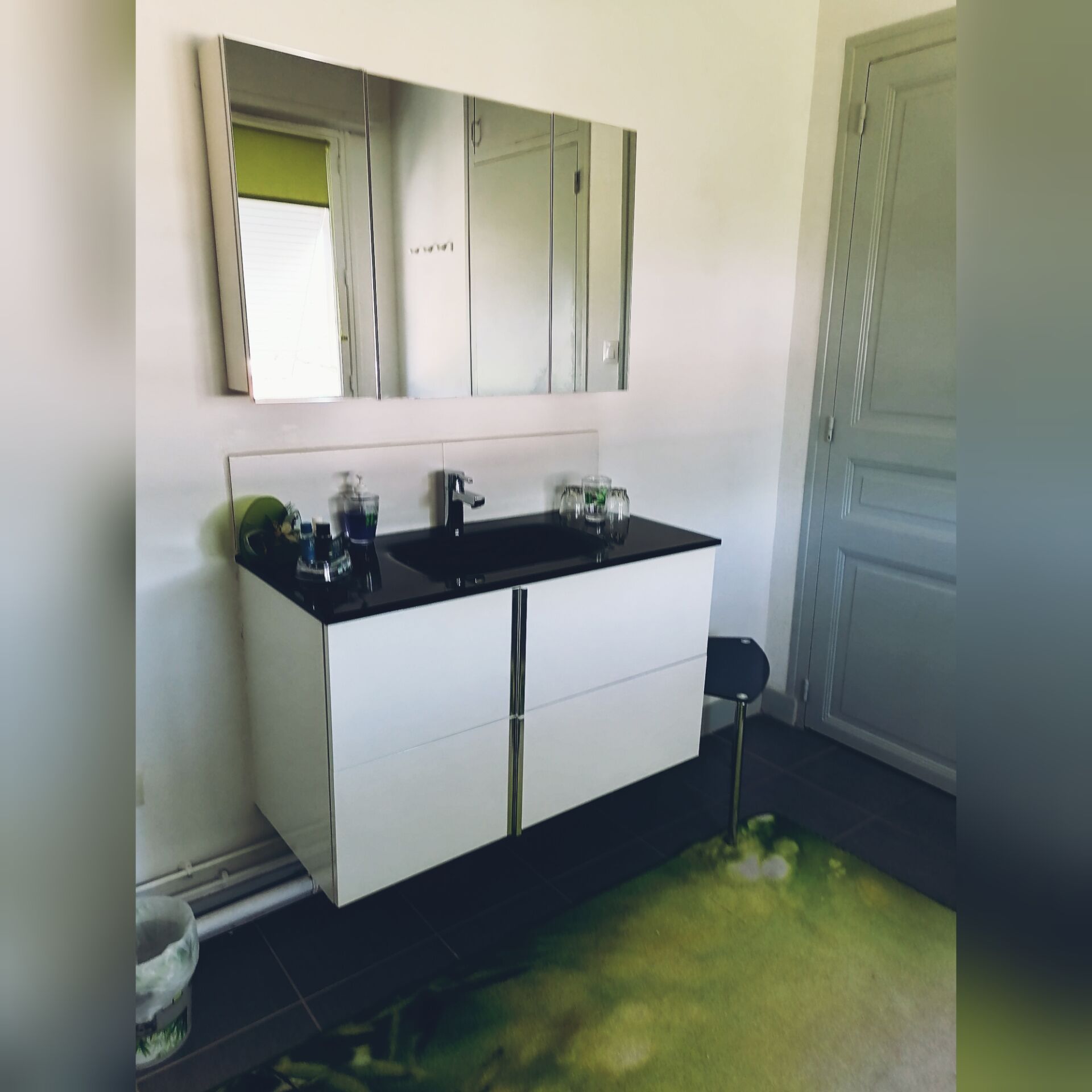 A modern bathroom with a large mirror, a black countertop, and a white cabinet.