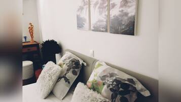 Una cama bien hecha con almohadas mullidas y un edredón blanco, una mesita de noche con una estatua, y una pared decorada con dos cuadros enmarcados.