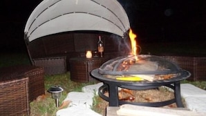 A fire pit with a tent structure in the background, surrounded by wicker furniture. - Le Clos des Mylandes (Dax)