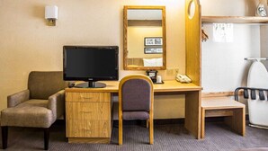 A hotel room with a wooden desk, a television, a chair, a small cabinet, a mirror, and a shower area. - Quality Inn Moab Slickrock Area (Moab)