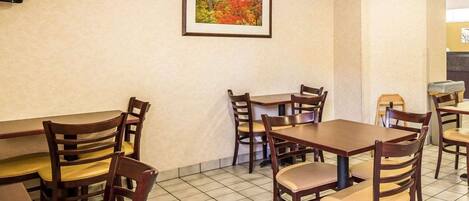 Un comedor con mesas y sillas de madera, un cuadro en la pared y piso de baldosas.