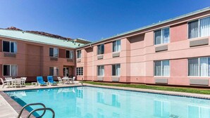 A swimming pool with lounge chairs and a building with multiple windows and air conditioning units. - Quality Inn Moab Slickrock Area (Moab)