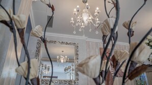 A grand room with a large mirror, ornate chandelier, and decorative plants.