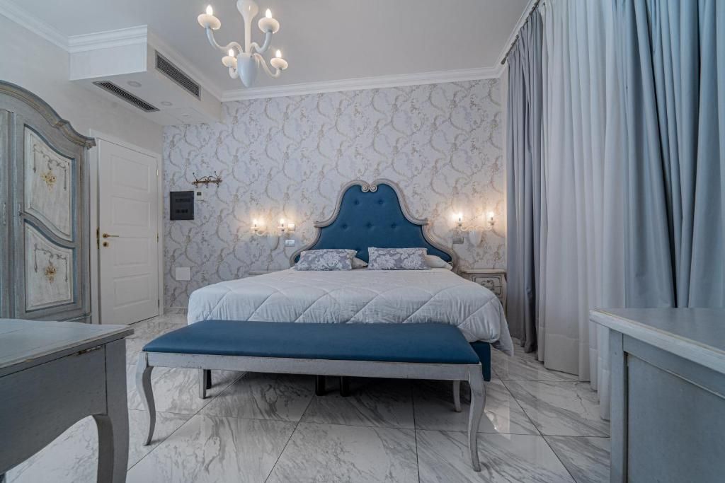 A bedroom with a large bed, a bench, a dresser, and a chandelier.