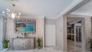 A spacious lobby with a marble floor, a large framed painting of a beach, a chandelier, and a modern door.