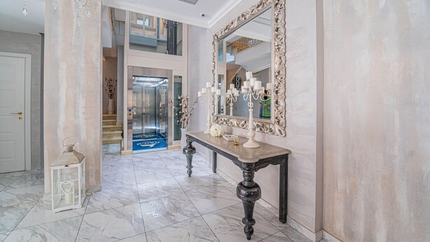 A grand hallway with a marble floor, a large ornate mirror, and a chandelier.