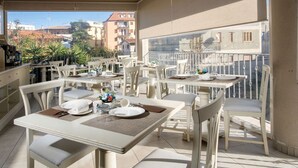 A sunlit outdoor dining area with white furniture and a view of buildings in the background.