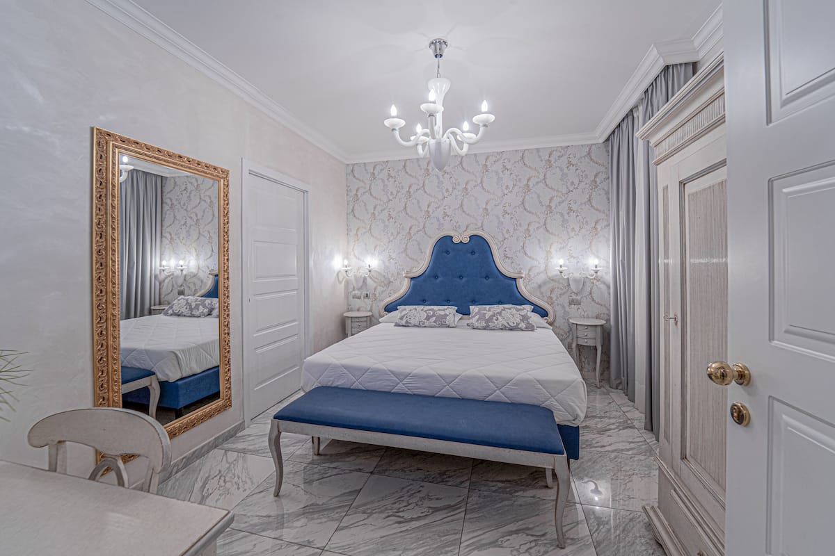 A bedroom with a large bed, a bench, a mirror, and a chandelier.