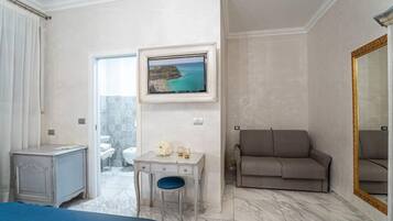 A hotel room with a bed, a desk, a chair, a sofa, a television, and a large mirror.