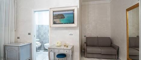 A hotel room with a bed, a desk, a chair, a sofa, a television, and a large mirror.