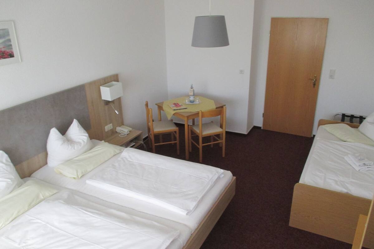 A hotel room with two beds, a desk with a chair, a lamp, and a door.