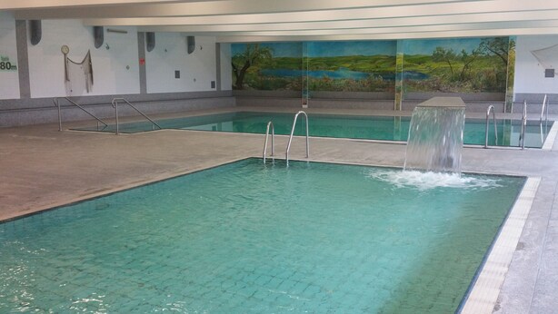 Una piscina interior con agua cristalina, un trampolín y un mural en la pared que muestra un paisaje.