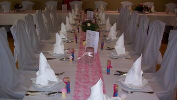 A banquet hall with round tables set for a formal event, featuring white tablecloths, neatly folded napkins, and a central floral arrangement.