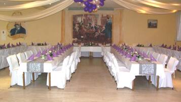 A banquet hall with long tables set for a formal event, draped with white tablecloths and purple napkins.