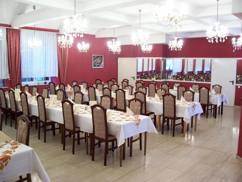 A banquet hall with multiple tables and chairs, chandeliers, and red walls.