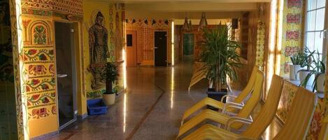 Um corredor com uma estátua de Buda, murais coloridos e fileiras de cadeiras de madeira.
