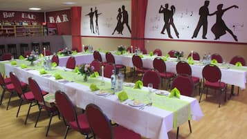 A banquet hall with tables set for dining, red chairs, and a bar area in the background.