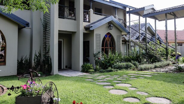 Un edificio a due piani con un balcone, una scala e un giardino con pietre decorative.