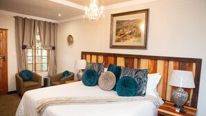 Camera d'albergo con un letto grande, due poltrone, una testiera in legno, un lampadario, un quadro e un comodino con una lampada.