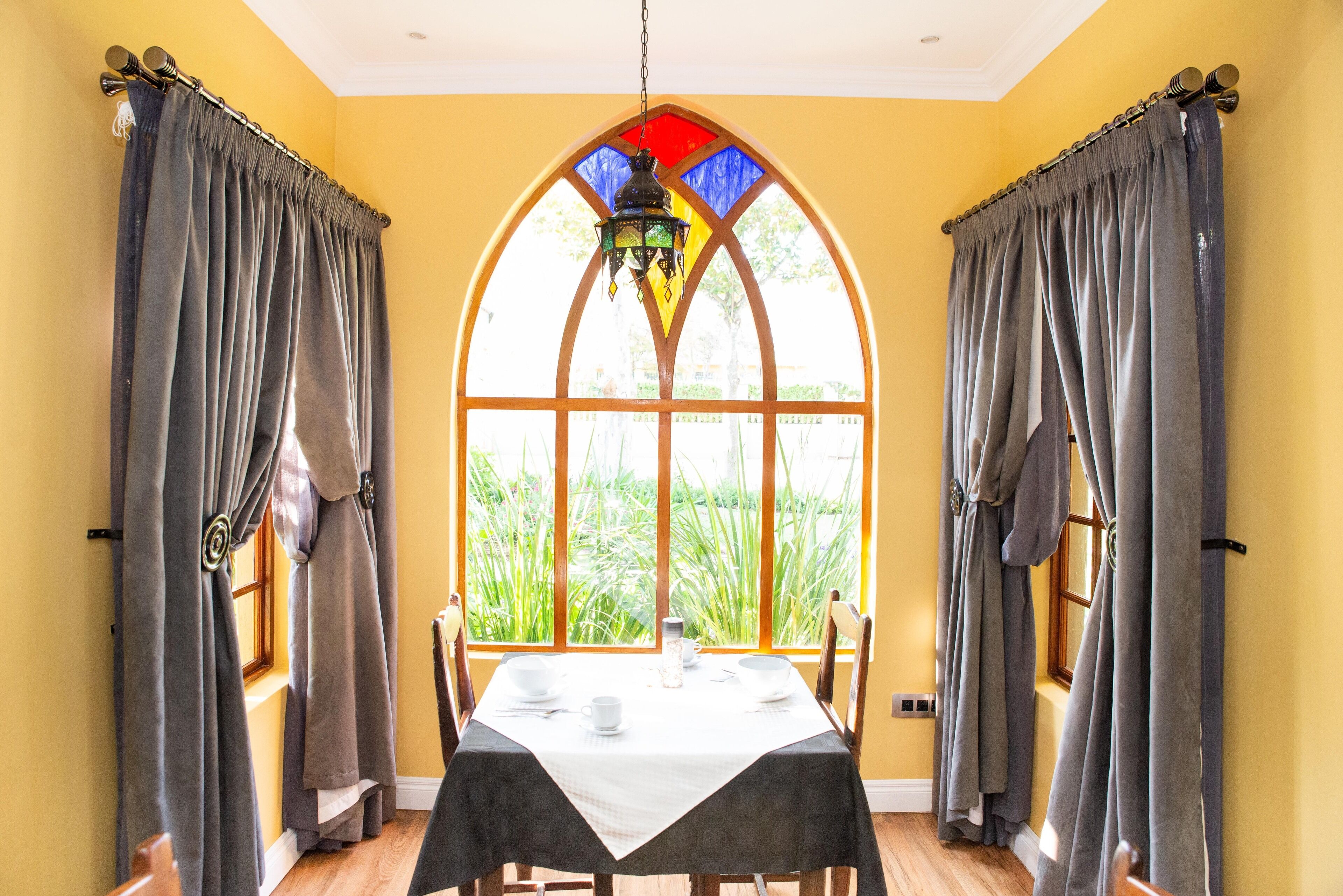A dining area with a table set for two, a stained glass window, and curtains.