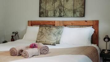 Ein ordentlich bezogenes Bett mit einem Holz-Kopfteil, zwei Kissen mit Weltkarten-Motiv und zusammengerollte Handtücher auf dem Bett.