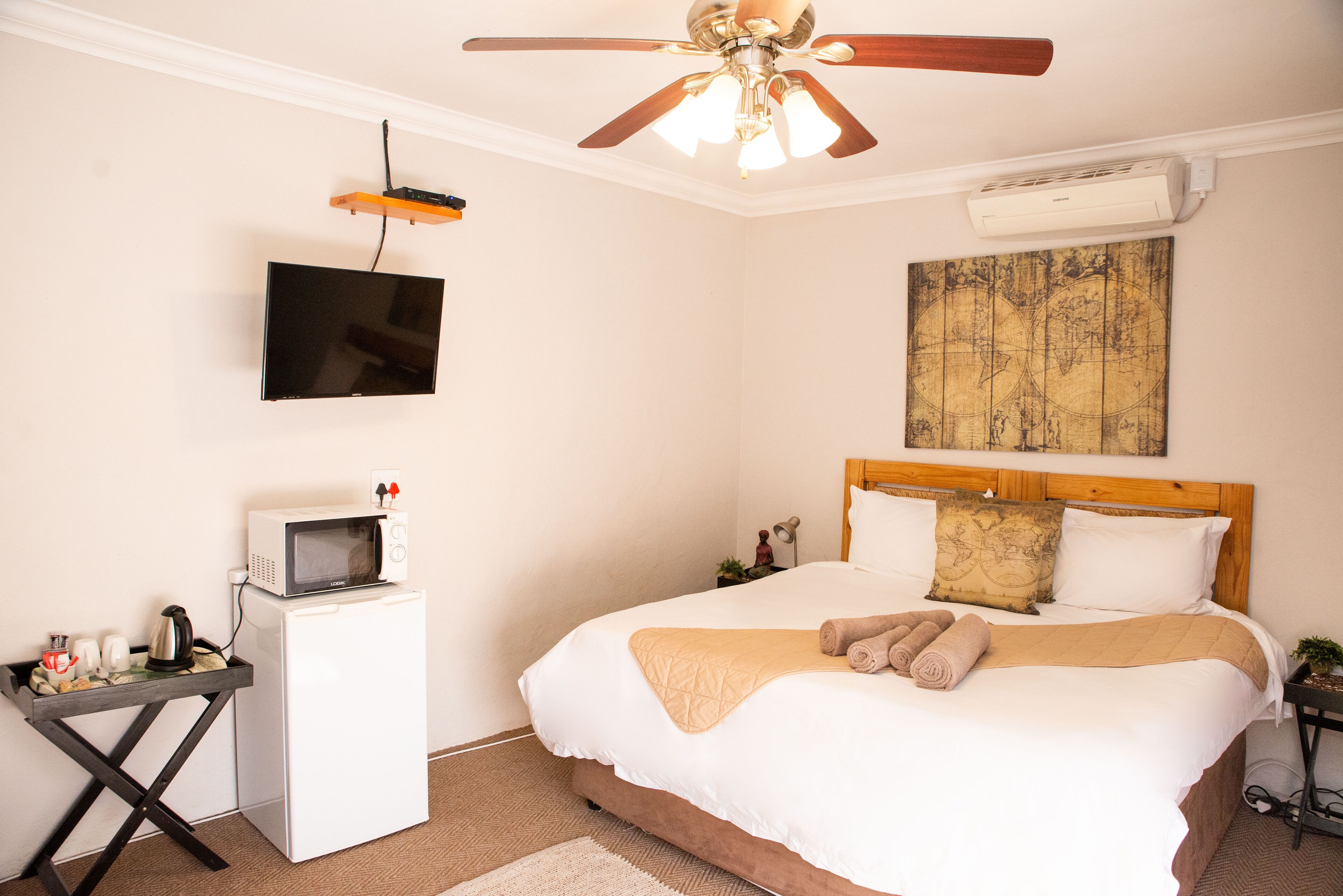 Une chambre avec un lit, un ventilateur de plafond, une télévision, un four à micro-ondes et une petite table avec une bouilloire et des tasses.