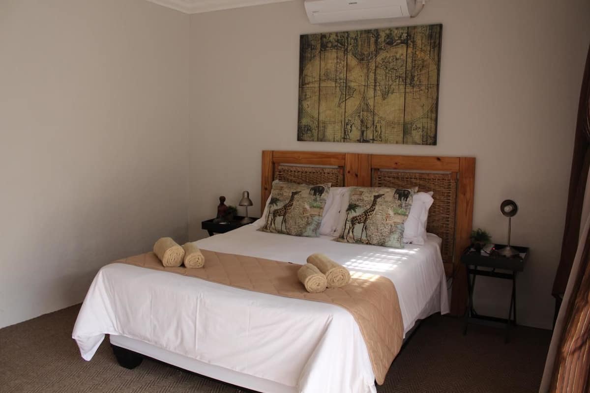 Cama bem arrumada com cabeceira de madeira, edredom bege e duas toalhas enroladas sobre a cama.