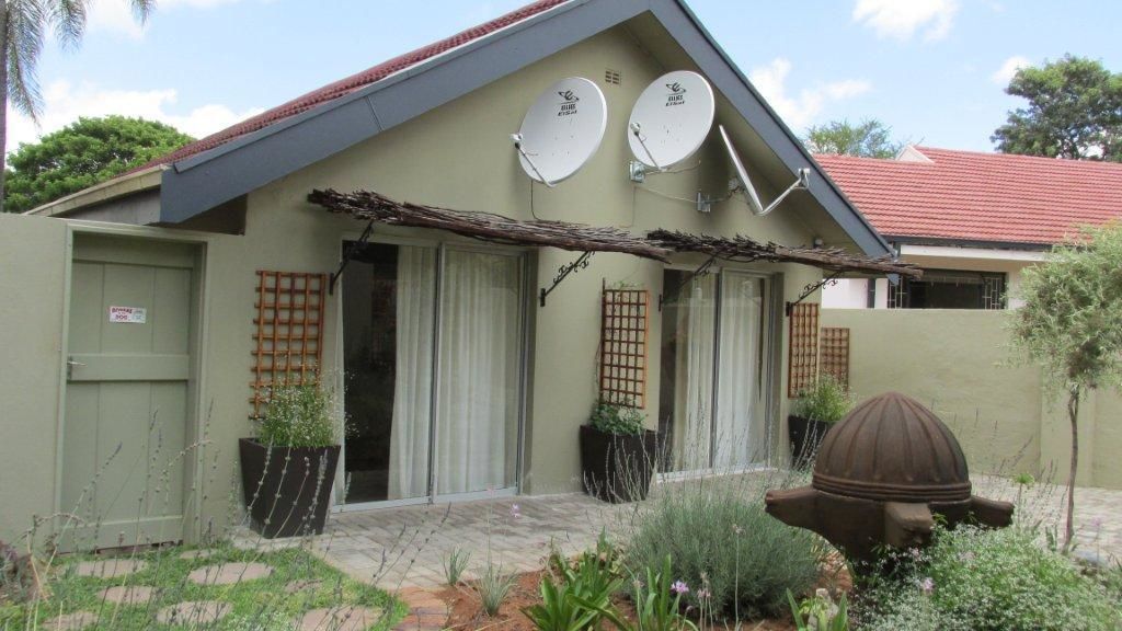 A house with satellite dishes, a garage door, and a garden with plants and a decorative object.