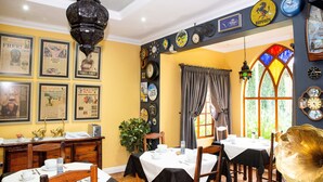 Zona pranzo con tavolo apparecchiato per due, un lampadario e una parete decorata con orologi e quadri.