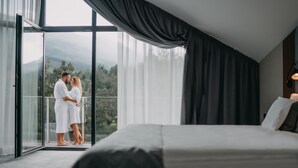 Un dormitorio con una cama grande, un balcón con vistas a las montañas y cortinas de gasa.