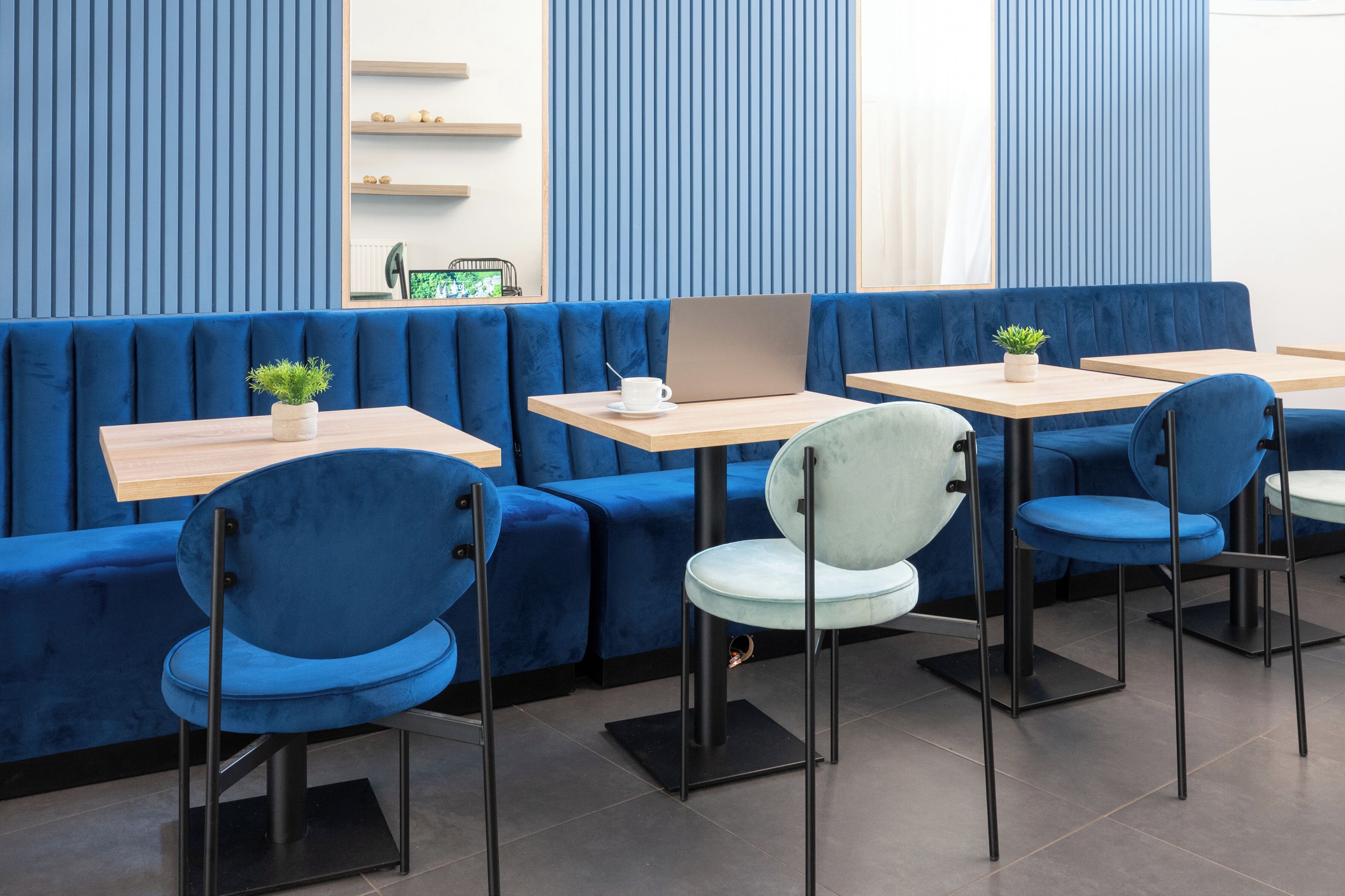 A modern restaurant with blue upholstered seating, wooden tables, and black metal chairs.