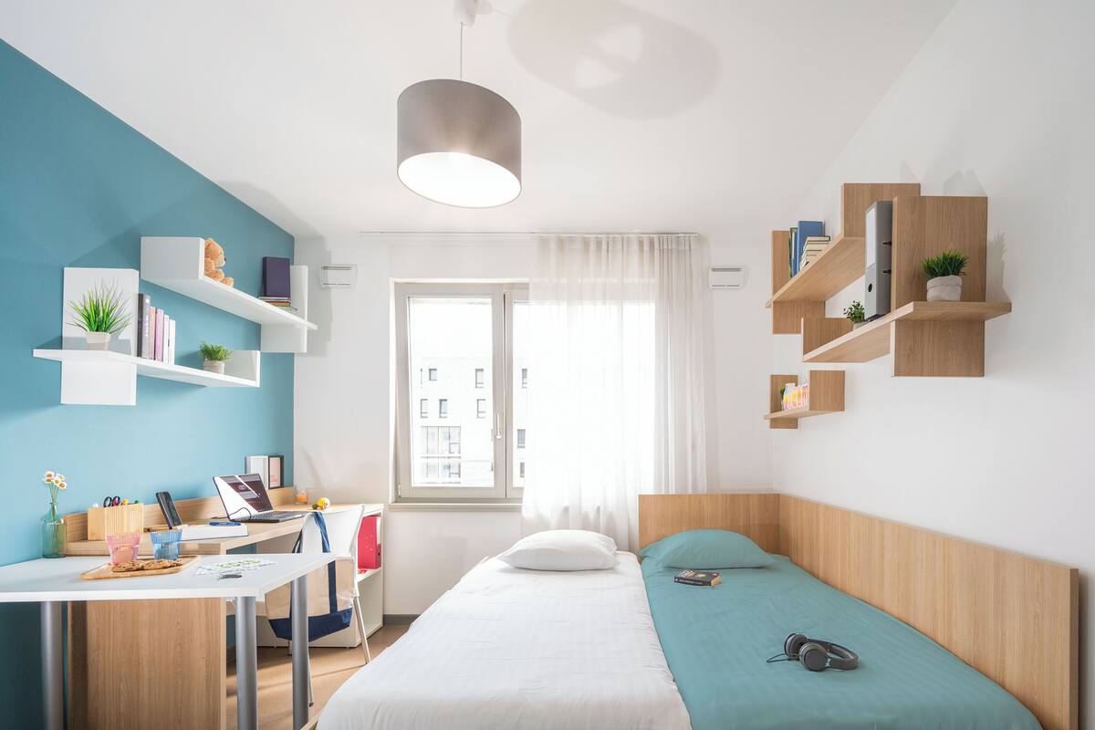 A modern bedroom with a bed, desk, and shelving units.