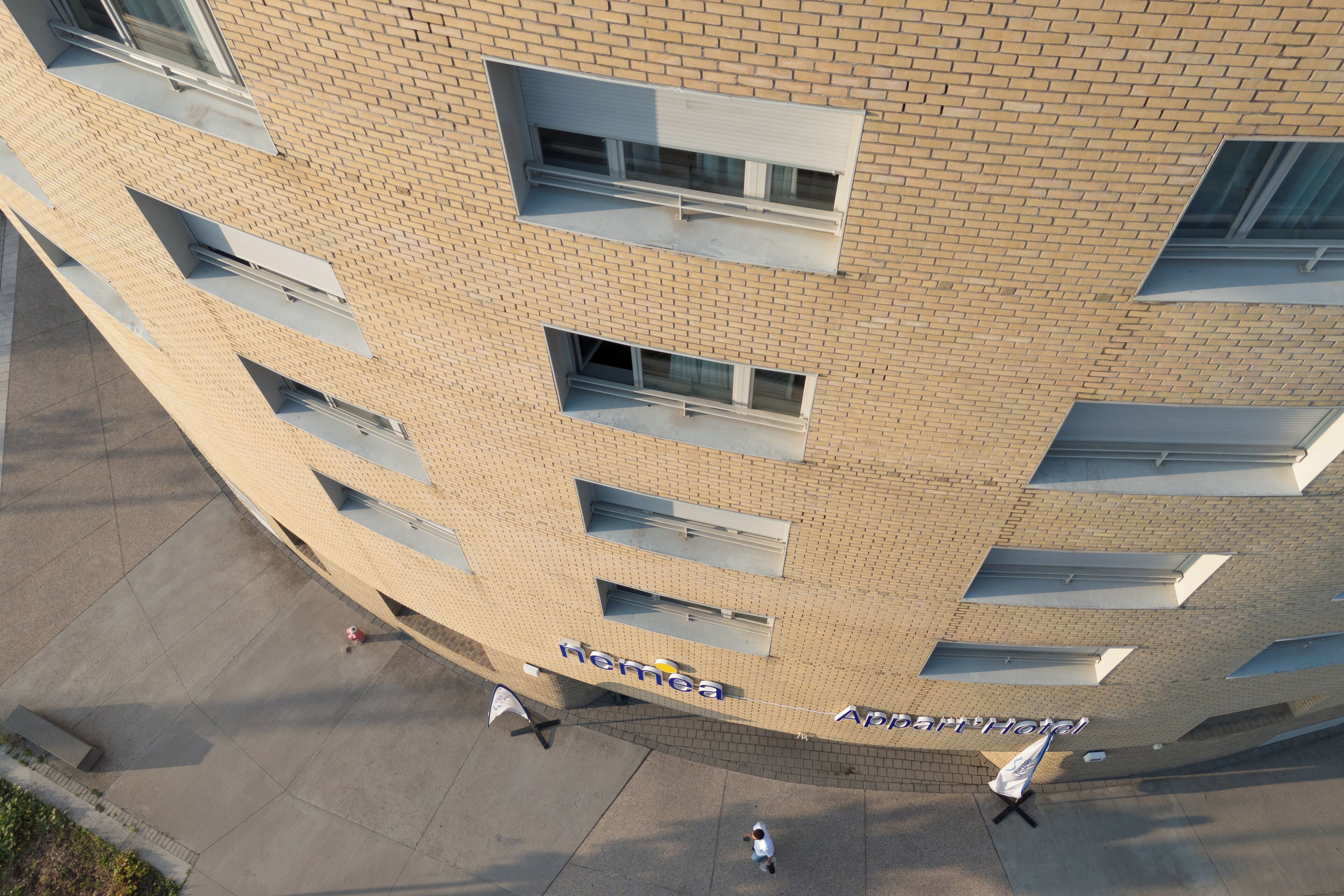Een meerlaags hotel met een bakstenen gevel, meerdere balkons en een duidelijk bord met de tekst 'Hema Apartments Hotel'.