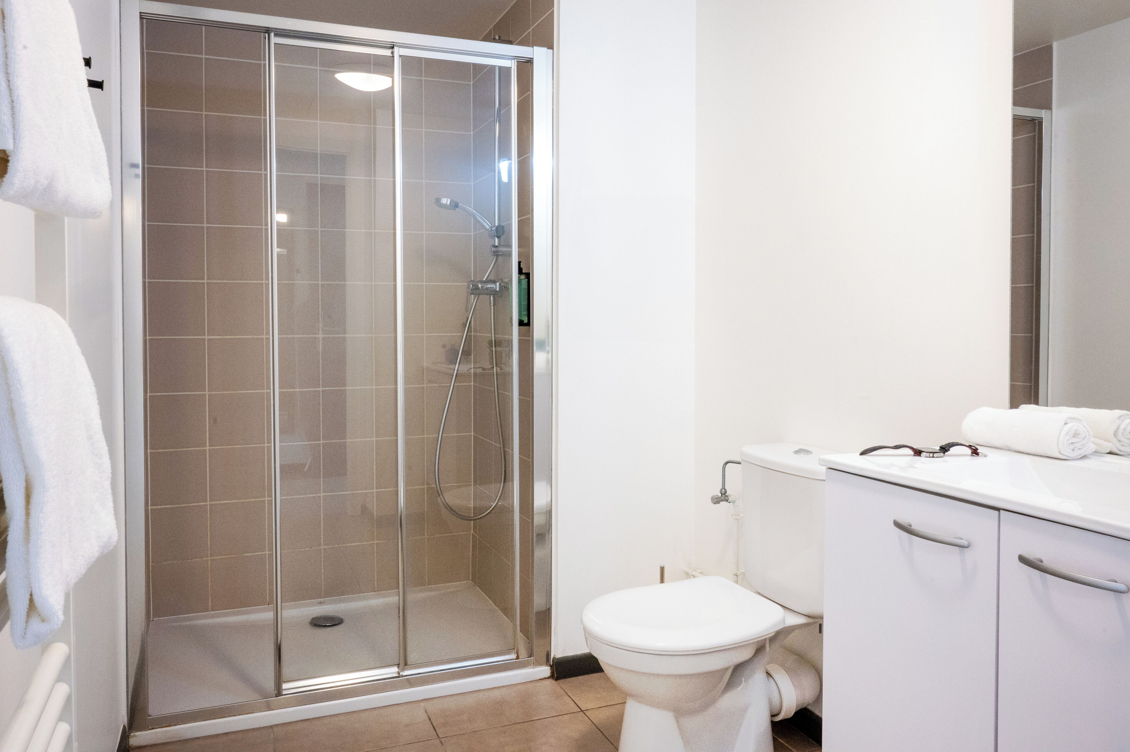 A modern bathroom with a glass-enclosed shower, a white toilet, and a white sink with a towel on the counter.
