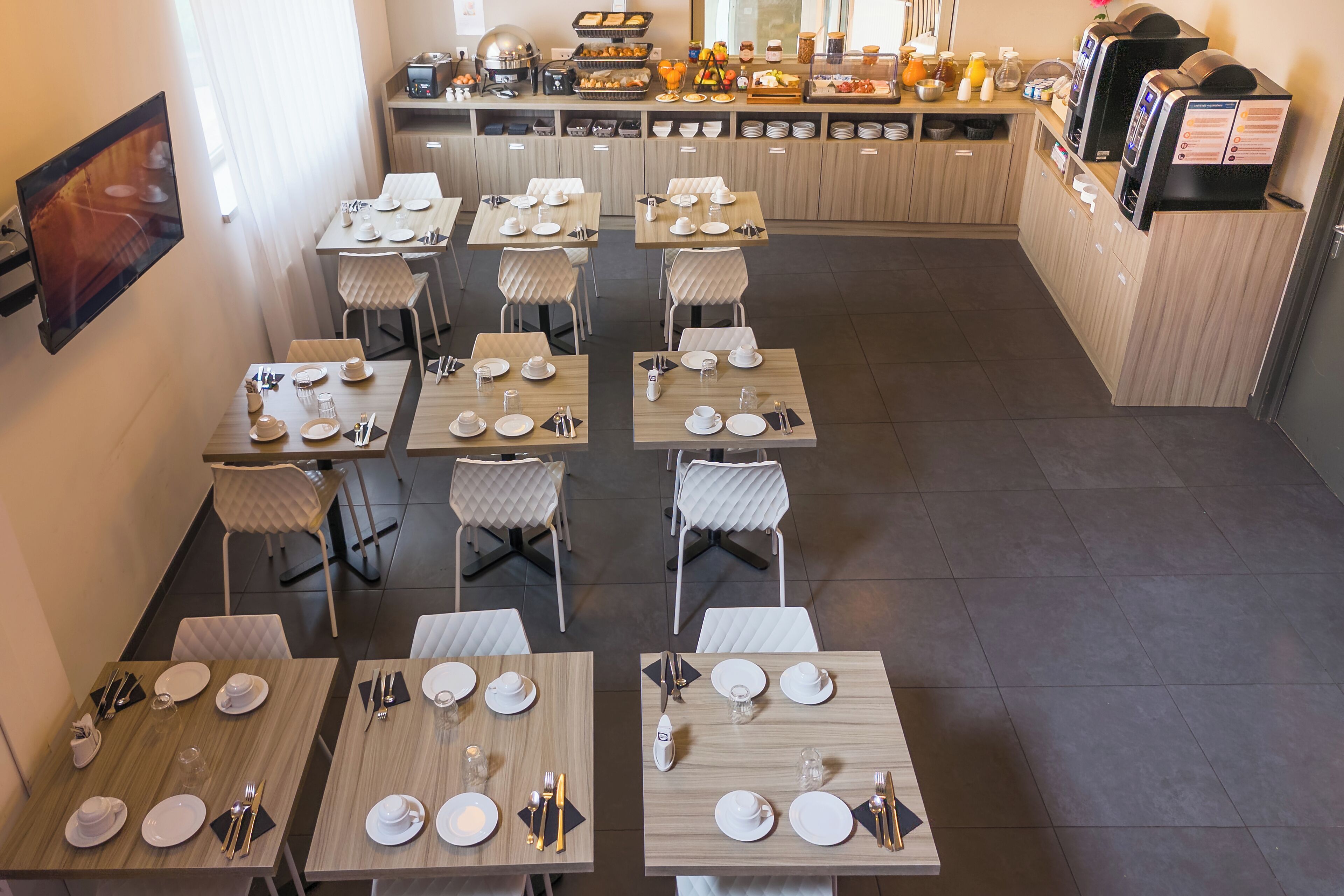 A restaurant with multiple tables set for dining, a buffet area in the background, and a coffee machine on the counter.