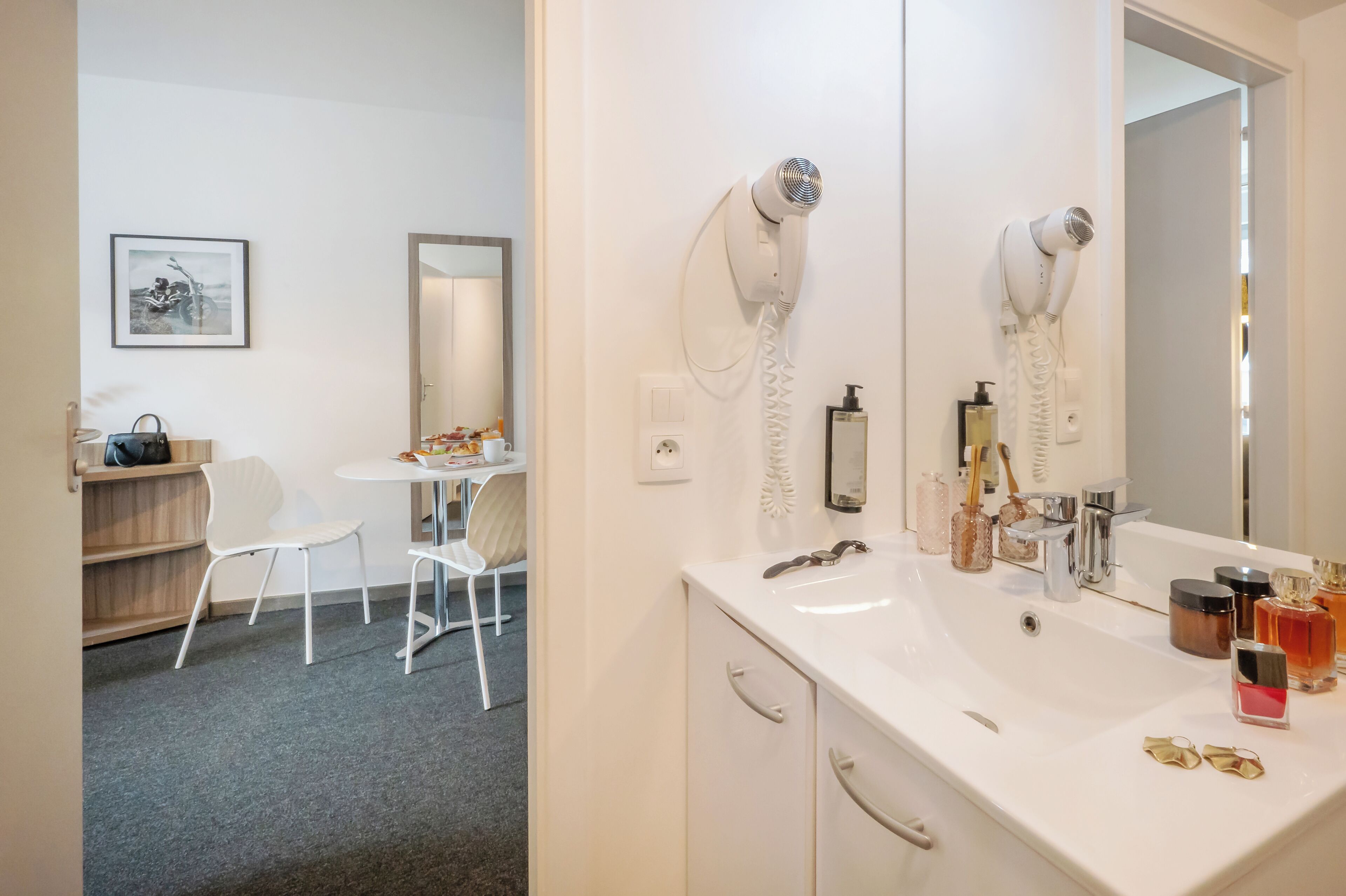 Et badeværelse med en hvid vask, to hårtørrere, et spejl og diverse toiletartikler.