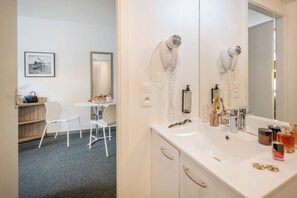 Ein Badezimmer mit einem weißen Waschbecken, zwei Haartrocknern, einem Spiegel und verschiedenen Pflegeprodukten.