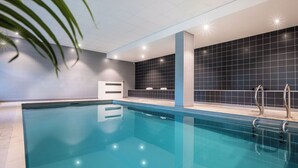 Una piscina interior moderna con agua cristalina, pared de azulejos azules y escaleras metálicas.