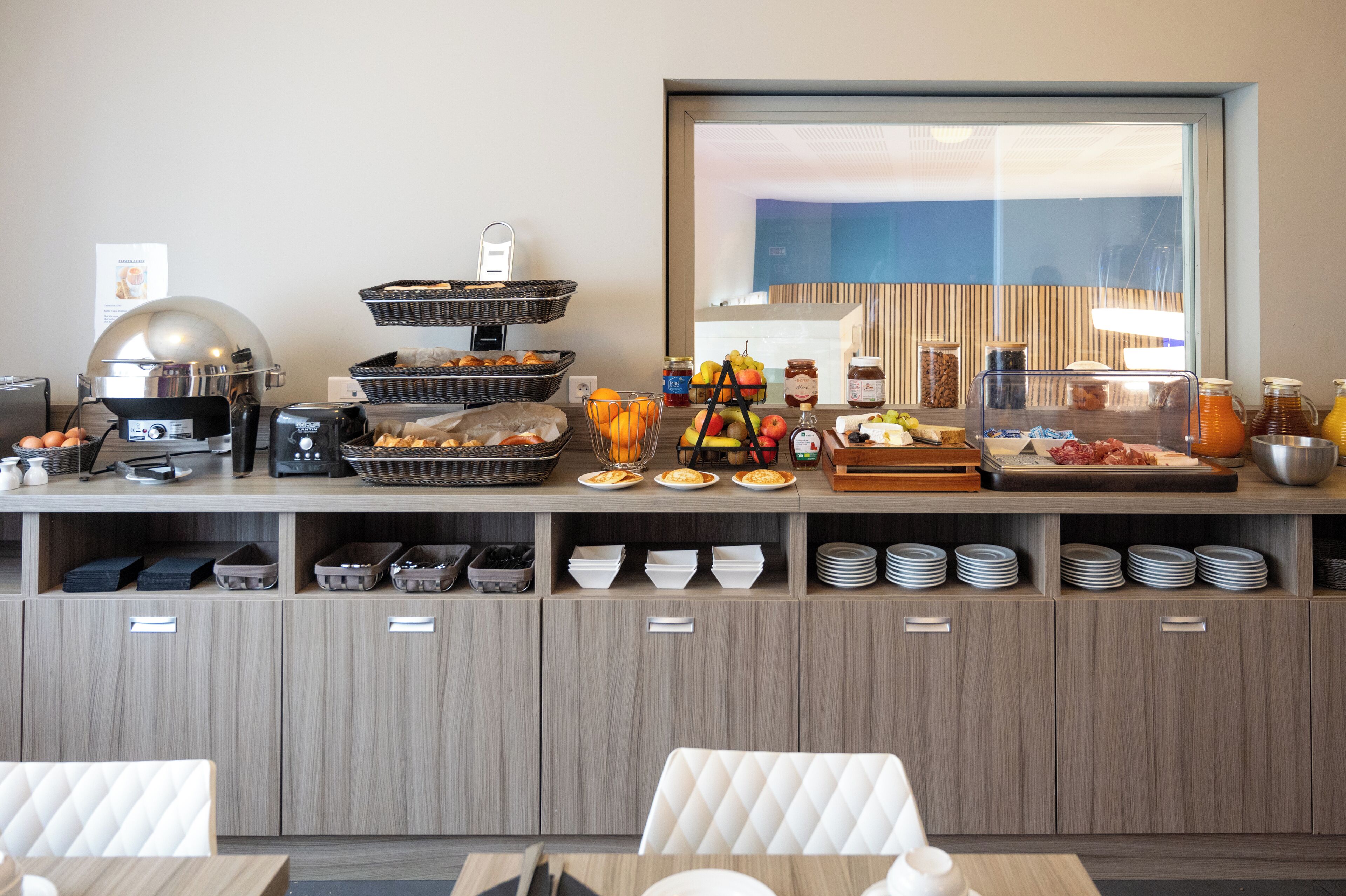 Een buffetopstelling met diverse gerechten, een koffieapparaat en een groot raam met uitzicht.