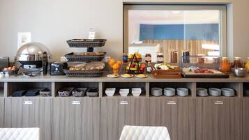 A buffet setup with various food items, a coffee machine, and a large window with a view.