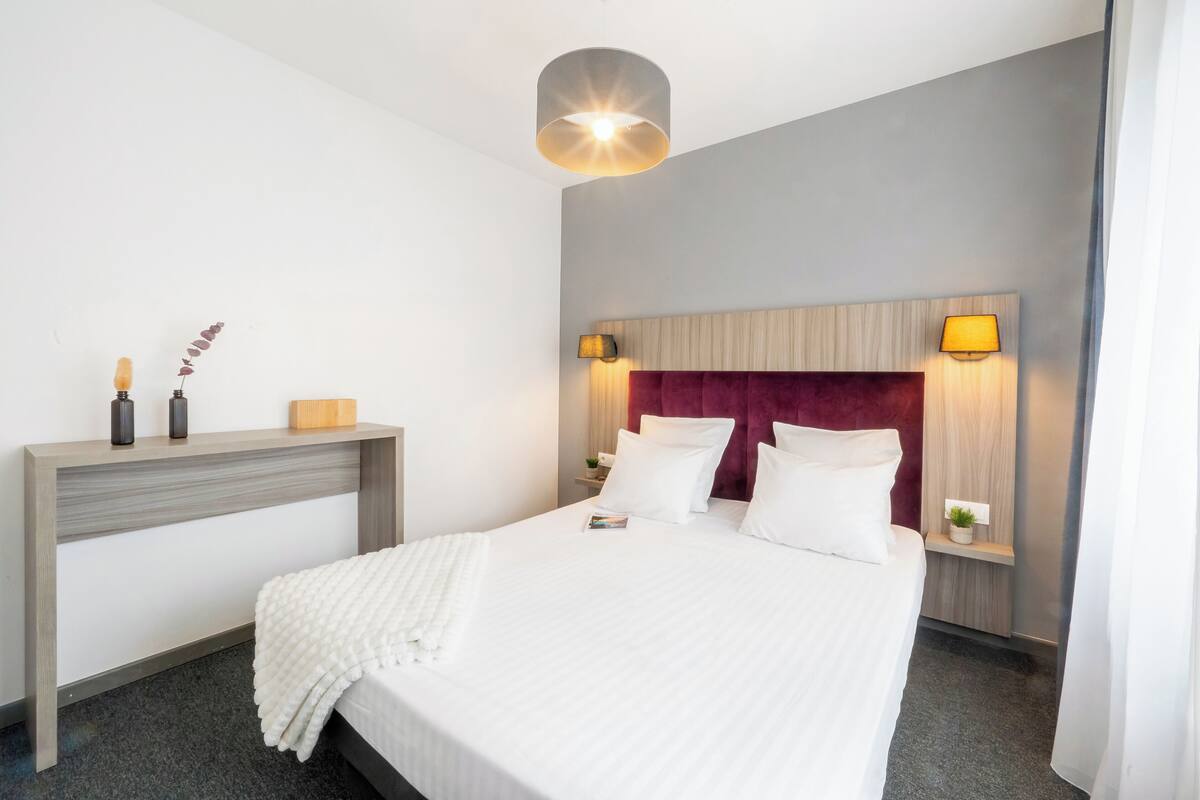 A hotel room with a large bed, a bedside table, two wall-mounted lamps, and a ceiling light.