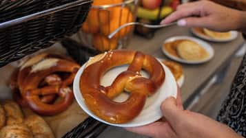 A person holding a pretzel with a basket of pretzels and a bowl of apples in the background.