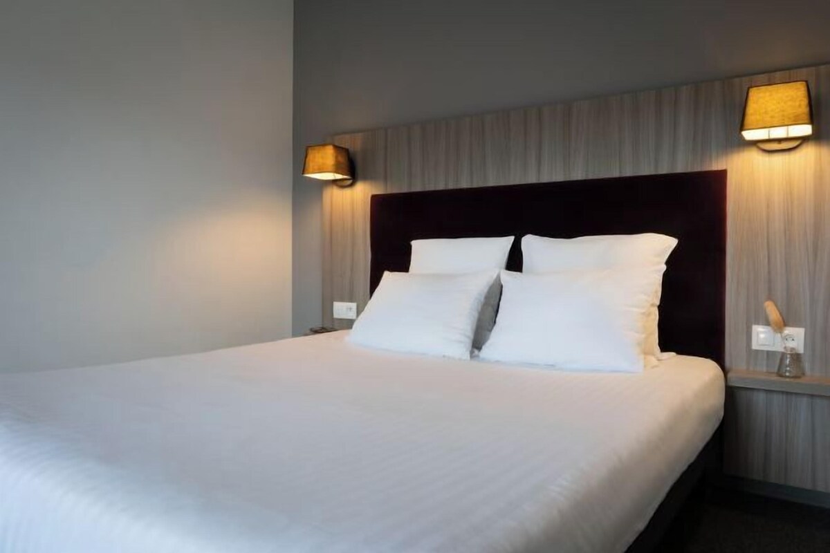 A hotel room with a large bed, two bedside lamps, and a nightstand with a lamp.