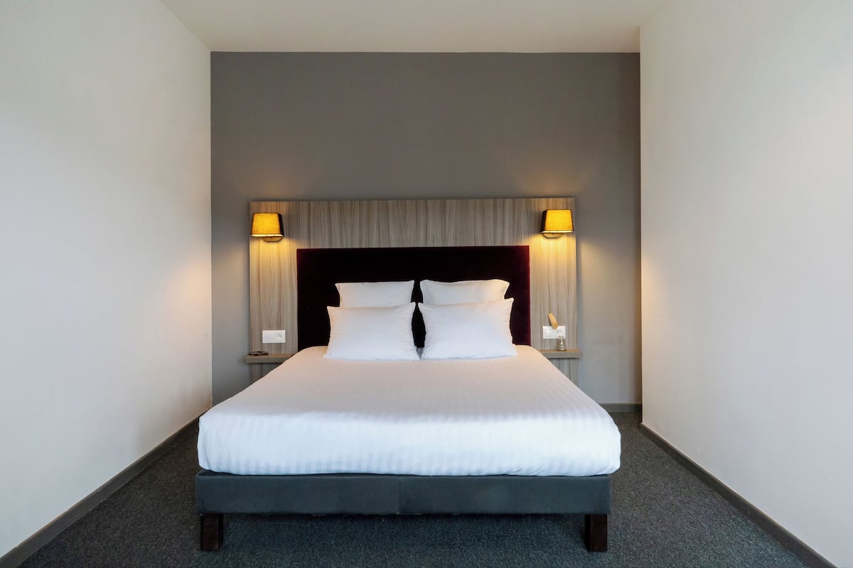 A hotel room with a large bed, two bedside lamps, and a headboard with a light-colored panel.