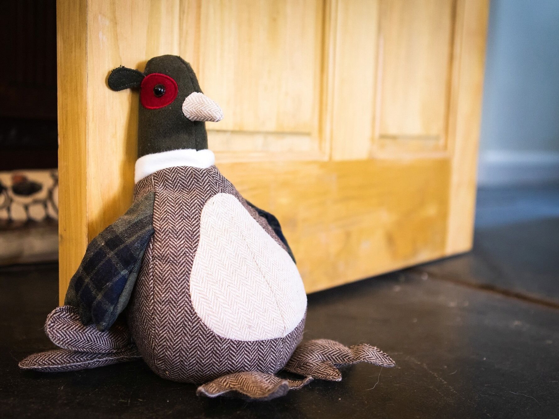 A plush toy penguin sitting on a dark floor with a wooden door in the background.