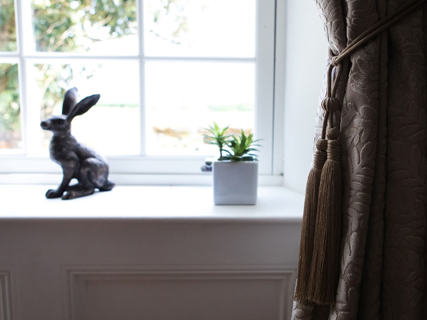 A window with a statue of a rabbit, a small potted plant, and a curtain.